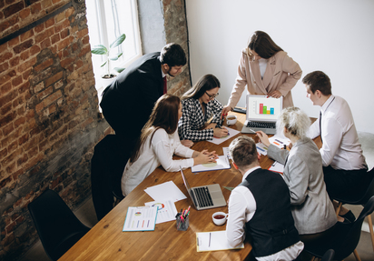 Mehrere Personen sitzen oder stehen um einen großen Tisch in einem Konferenzraum und erarbeiten etwas im Team