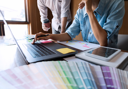 Eine Person arbeitet an einem Schreibtisch, hinter ihr steht eine weitere Person