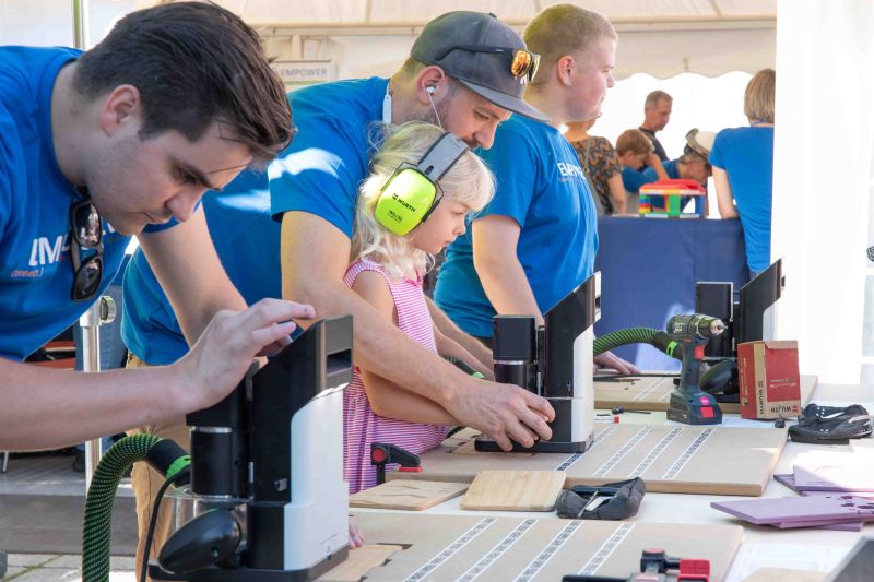 EMPOWER-Mitarbeiter mit einer kleinen Besucherin beim Anfertigen eines Brettchens.