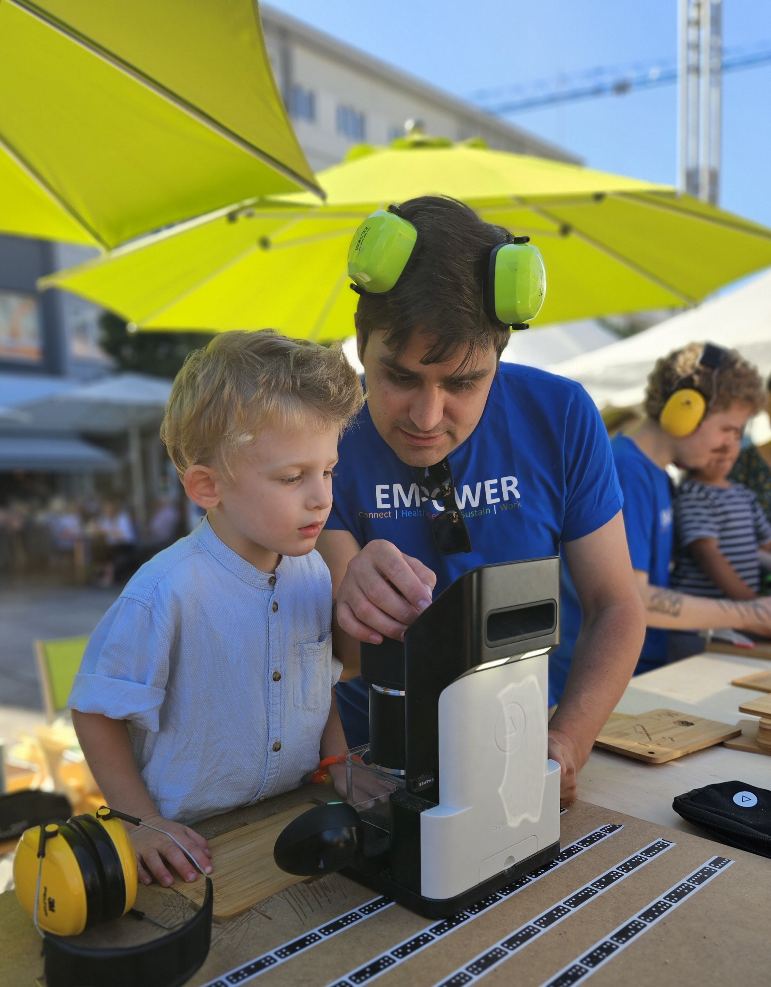 EMPOWER-Mitarbeiter mit einer kleinem Besucher beim Anfertigen eines Brettchens.